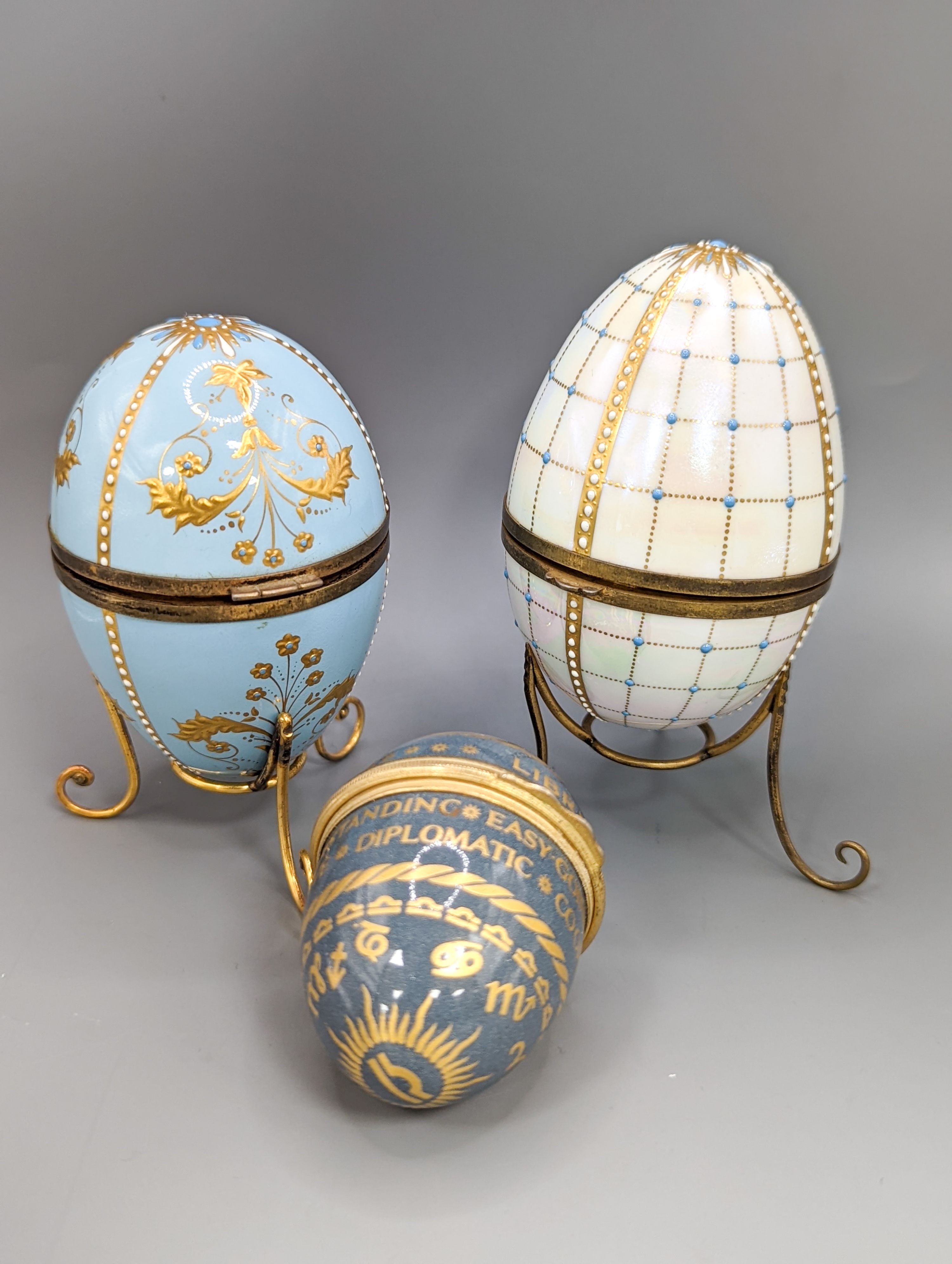Two silver gilt mounted enamelled eggs with interior seascapes, on silver gilt stands, Birmingham, 1985 & 7 and a smaller similar gilt metal mounted zodiac egg, tallest 8.5cm